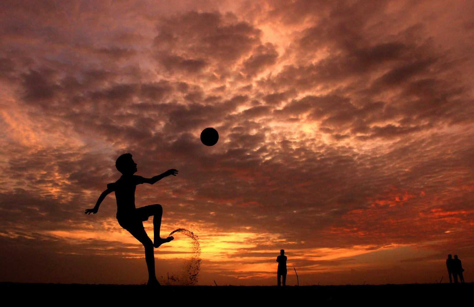 A child playing soccer on the beach at sunset in Kochi, India, creating a striking silhouette against the vibrant sky.